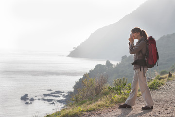 femme qui fait des photos de la mer en randonnant avec un sac à dos 