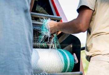 Cropped shot of two male farmworkers untangling netting in hay baler