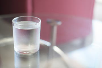 Cold glass of water put on glass table (focus at edge of glass)