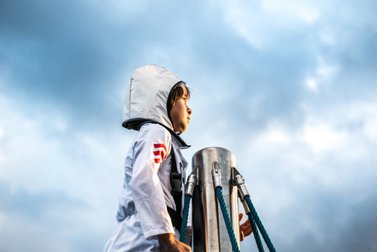 Portrait of boy in astronaut costume gazing out from top of climbing frame against dramatic sky