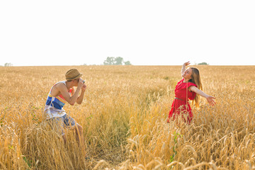 Male photographer taking pictures of a young woman standing in field. Couple enjoying day on nature
