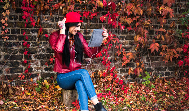 Portrait of young woman sitting outdoors, wearing earphones, using digital tablet