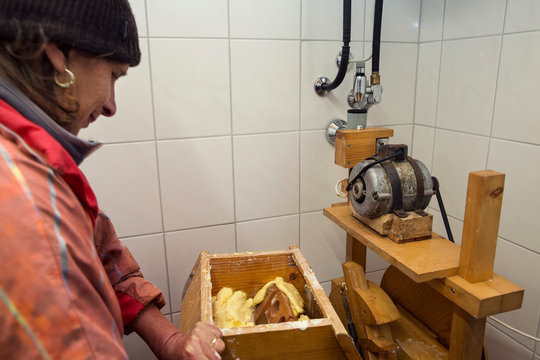 Senior female dairy farmer churning butter in dairy farm kitchen, Sattelbergalm, Tyrol, Austria