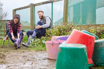Young couple on farmland putting on rubber boots