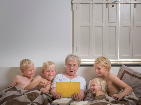 Grandmother in bed with grandsons using digital tablet