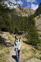 Naklejka na ściany i meble femme souriant avec un sac à dos qui marche dans la montagne avec un gros pull