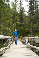 Fototapeta na wymiar femme souriant qui marche sur un pont en bois dans la forêt avec un sac à dos