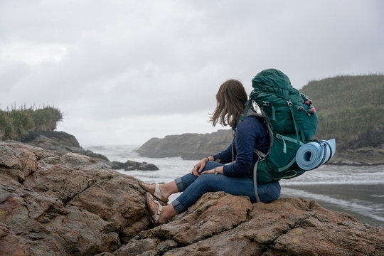 Young woman with backpack, sitting on rock, Constant Bay, Charleston, South Island, New Zealand