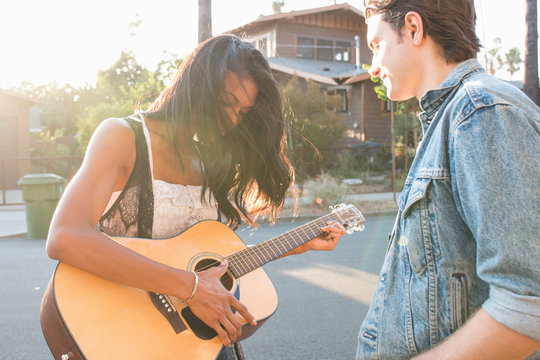 Young couple outdoors, young woman playing guitar