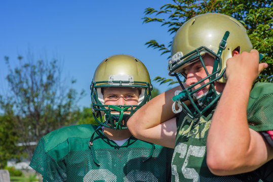 Two teenage male American football players putting on helmets at playing field