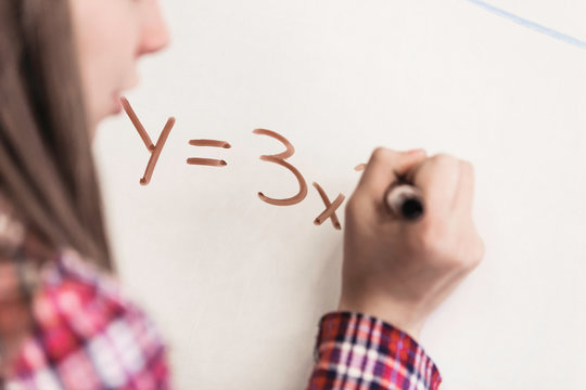Close up of teenage girl writing equation on whiteboard at school