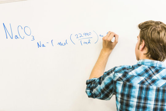 Rear view of teenage boy writing equation on whiteboard in high school lesson