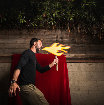 Man holding cardboard cut-out of flames pretending to breathe fire