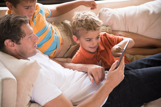 Man and two sons pointing at digital tablet on sofa