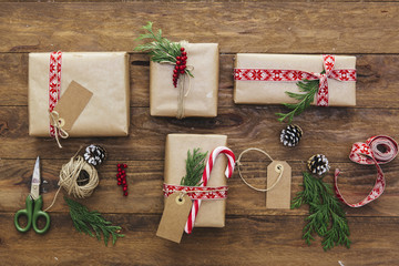 Overhead view of wrapped Christmas gifts with a gift tag and rustic fir, pinecone, candy cane and ribbon decorations on a wooden table 