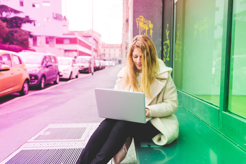 Young beautiful caucasian blonde hair woman sitting outdoor using computer and smart phone - small business, technology, student concept - colorful filtered