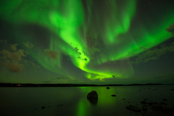 Obraz na płótnie Canvas Northern Night Sky - Bright aurora Borealis spreading cross the starry night sky over a lake.
