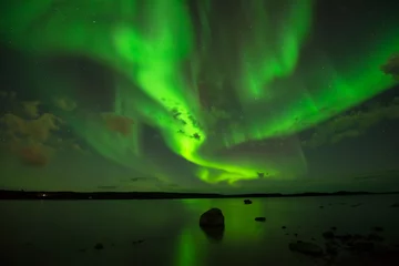 Fotobehang Northern Night Sky - Heldere aurora Borealis verspreidt zich over de sterrenhemel boven een meer. © Sean Xu