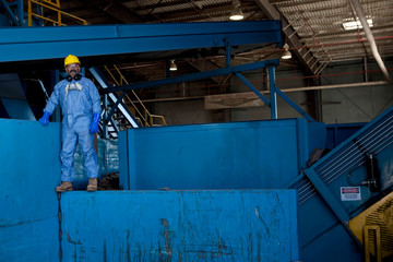 Portrait of male worker in hard hat standing on blue heavy machinery at recycling plant