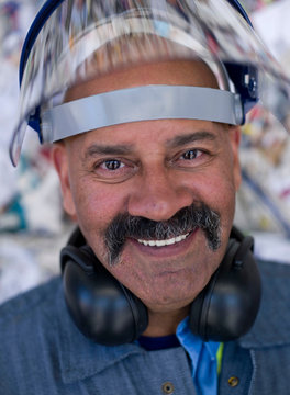 Portrait of male worker in hard hat visor, in front of rubbish at recycling plant