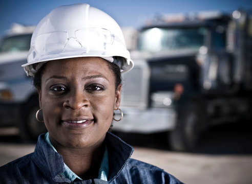 Portrait of female worker in hard hat in front of recycling plant trucks