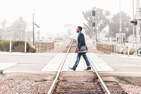 Young man walking across level crossing, side view