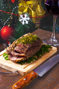 cold boiled pork on a wooden board with a glass of red wine on the background of Christmas tree