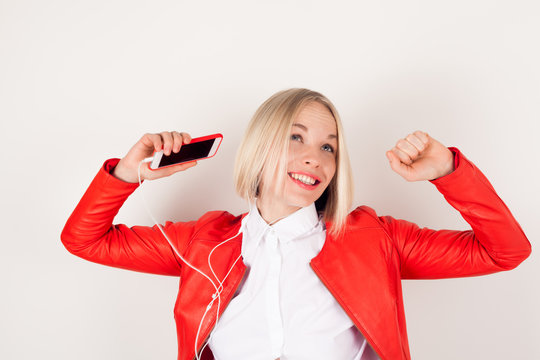 Portrait of a woman with headphones and mobile phone in hand in red jacket on white background. The emotion of happiness. Girl dancing to the music
