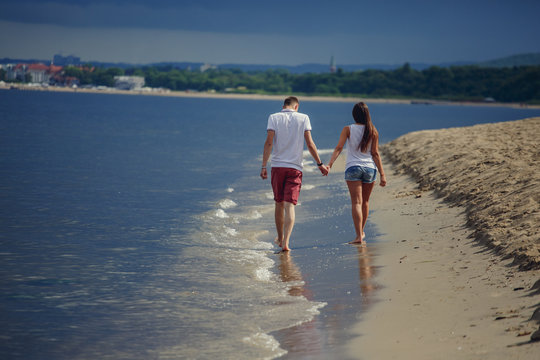 Rear view of a couple walking on the beach, holding hands. Horizontal shot.