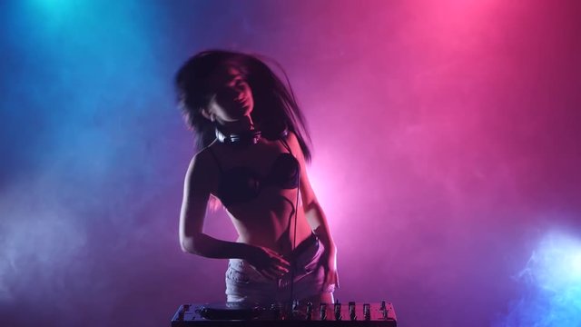 Girl dj hand spinning a dj stand, behind her pink blue lights in smoke