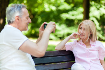 Senior couple taking a picture in the park seated on a bench