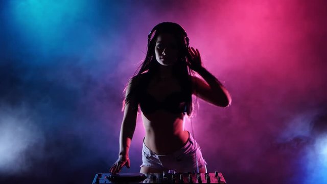 Girl DJ dancing develop her hair behind her multicolored lights and smoke. Silhouette