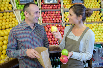 Shop assistant showing man three varieties of apple