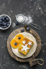 Two servings of homemade juicy mandarin biscuit with asterisks from icing sugar on a dark background. Top view