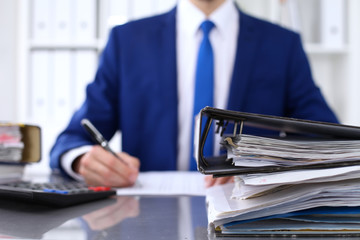 Binders with papers are waiting to be processed with businessman back in blur. Accounting planning...