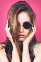 Beautiful fashionable woman in black sunglasses. Pink background. Girl in sunglasses. Round glasses. Toned image.