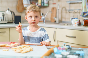 Little blond kid tries freshly baked shortbread, sitting at the kitchen table. Grimacing face.