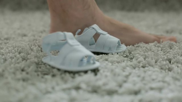 Two children's sandals close to a man's foot.