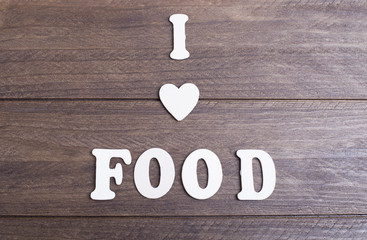 White letters laying on dark wood messaging I love food. Horizontal studio shot