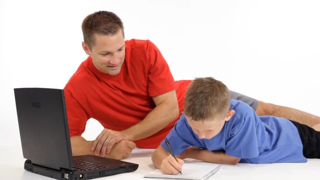 A father and his son lying on the floor and using a laptop to help with homework