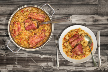Plateful of Cabbage Cooked with Smoked Pork Ribs in Stainless Steel Saucepot Served on Old Rustic Cracked Flaky Wooden Garden Table