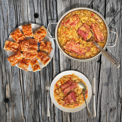 Plateful of Cooked Cabbage with Smoked Ribs Served in Steel Saucepot and Gibanica Crumpled Cheese Pie Set on Old Cracked Rustic Pine Wood Garden Table 