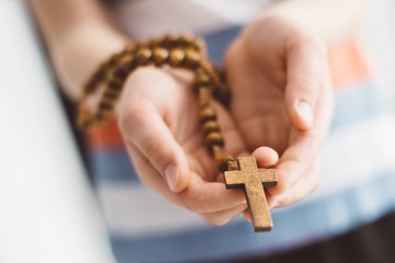 Little boy child praying and holding wooden rosary. - obrazy, fototapety, plakaty