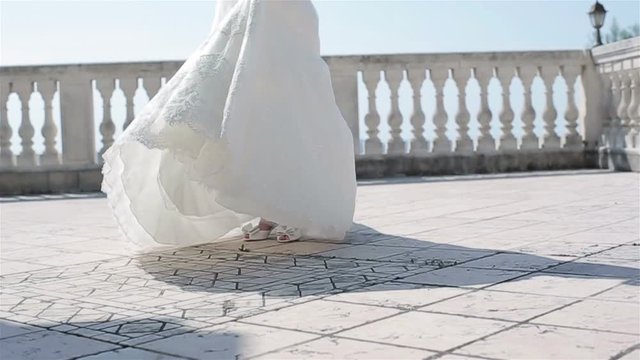 Woman in white dress spinning outdoors no face slow motion low angle. Bride in lace gown dance turning around on terrace balcony floor holding embroidered hem celebrating marriage wedding fashion show