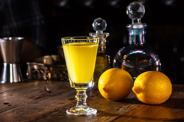 glass of Limoncello is on the table in  dark room. In the bac