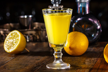 glass of Limoncello is on the table in  dark room. In the bac