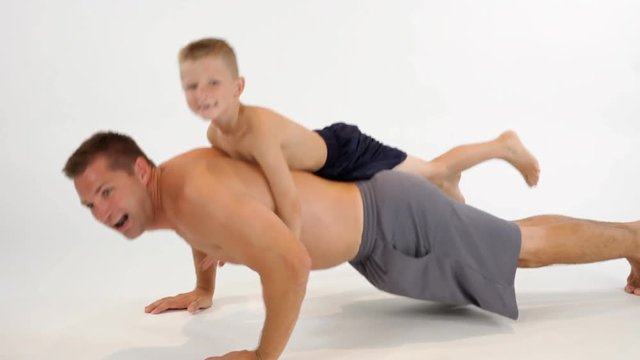A young muscular father performs a set of push-ups with his seven year old son on his back.