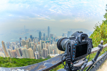 Obraz premium Close up of a professional camera on the tripod while photographing the Victoria Harbour from The Victoria Peak in Hong Kong. Fisheye lens with focus on the camera and background skyline blurred.