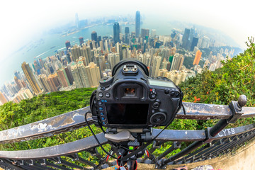 Fototapeta na wymiar Close up of a professional camera on the tripod while photographing the Victoria Harbour skyline from Lugard Road Lookout at Victoria Peak, the highest mountain in Hong Kong Island. Fisheye lens.
