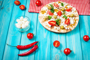 Pita with cheese, cherry tomatoes, olives and greenery on blue wooden background.